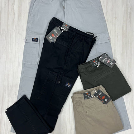 Four pairs of pants in gray, black, and beige with tags on a light wooden floor.