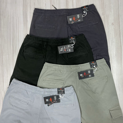 Four pairs of pants in black, gray, and green with tags on a light wooden surface.